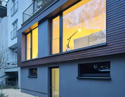 Gebäude teilweise mit Holzfasade und erleuchteten Fenstern am Abend