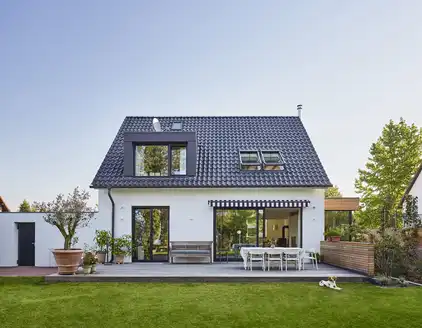 zweistöckiges weißes Haus mit dunkelblauem Spitzdach, Terrasse, Garten am Tag