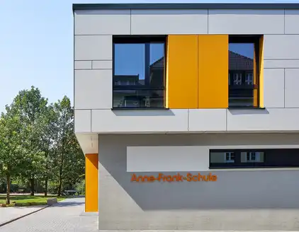 graues Gebüude mit Aufstockung, gelbe Akzente in Fassade