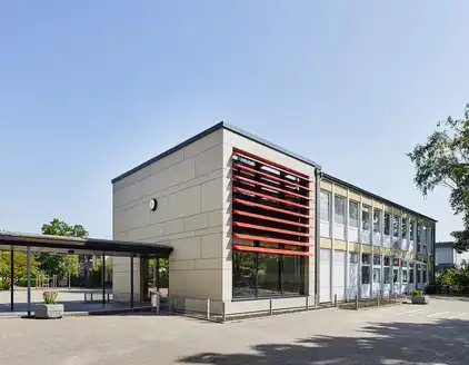 Schule mit roten Lamellen an Fensterfront, überdachter Weg zu Nebengebäude
