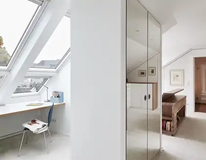 Helles Zimmer mit Schreibtisch unter Fensterfront, Schrank in der Mitte, Durchgang zu Schlafzimmer rechts