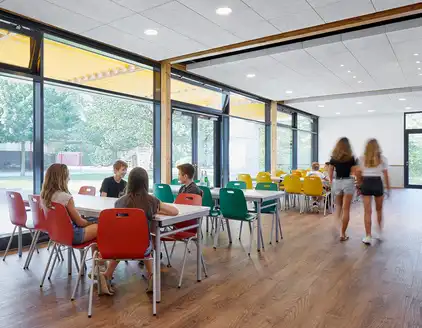 Mensa mit weißen Tischen, bunten Stühlen, Holzboden, Fensterfront