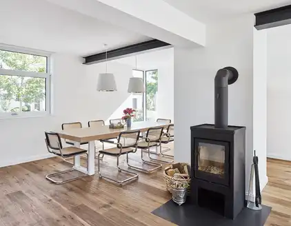 heller Raum mit Tischgarnitur links und schwarzem Ofen in der mitte