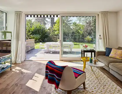 Wohnzimmer mit Sofa rechts und Blick auf Fensterfront zur Terrasse hinaus