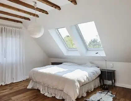 Schlafzimmer mit Holzdeckenbalcken, Doppelbett in der Mitte, Blich auf Dachfenster