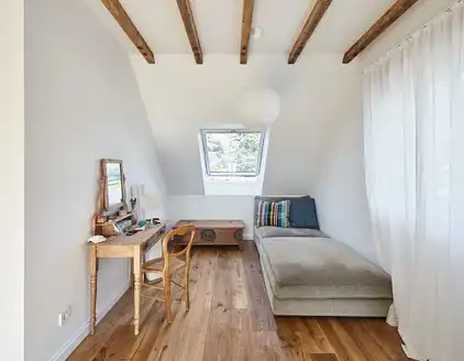 kleines Zimmer mit Schlafsofa rechts und Schreibtisch links, Blick auf ein Dachfenster