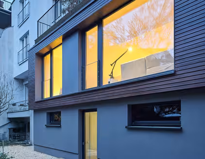 Gebäude teilweise mit Holzfasade und erleuchteten Fenstern am Abend