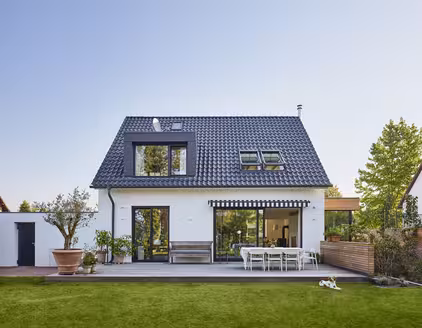 zweistöckiges weißes Haus mit dunkelblauem Spitzdach, Terrasse, Garten am Tag