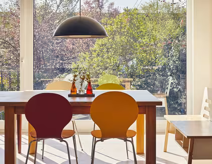 Tischgarnitur mit Holztisch und bunten Stühlen, Blick durch Fensterfront auf Garten