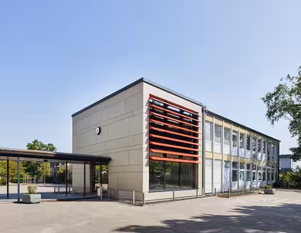 Schule mit roten Lamellen an Fensterfront, überdachter Weg zu Nebengebäude