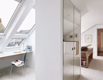 Helles Zimmer mit Schreibtisch unter Fensterfront, Schrank in der Mitte, Durchgang zu Schlafzimmer rechts