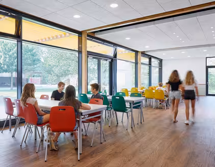 Mensa mit weißen Tischen, bunten Stühlen, Holzboden, Fensterfront