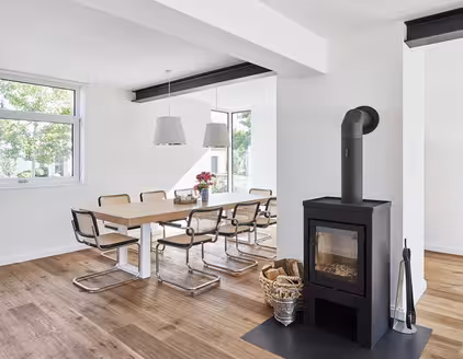 heller Raum mit Tischgarnitur links und schwarzem Ofen in der mitte