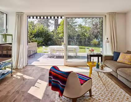 Wohnzimmer mit Sofa rechts und Blick auf Fensterfront zur Terrasse hinaus