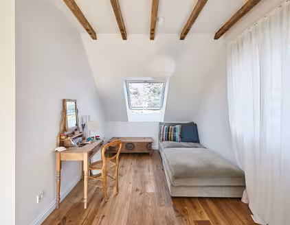 kleines Zimmer mit Schlafsofa rechts und Schreibtisch links, Blick auf ein Dachfenster