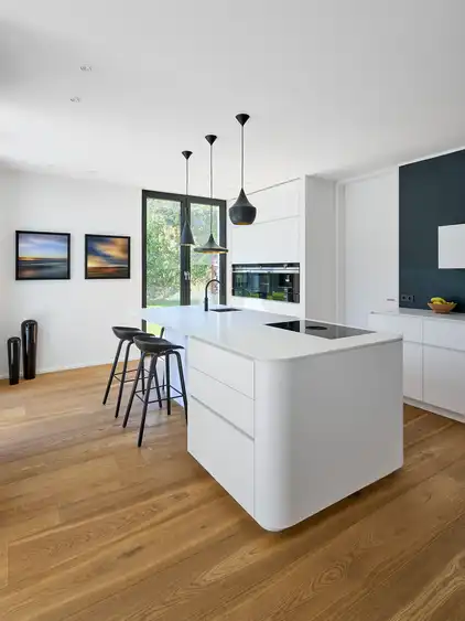 helle Küche mit weißer Kücheninsel und dunklen Hängelampen