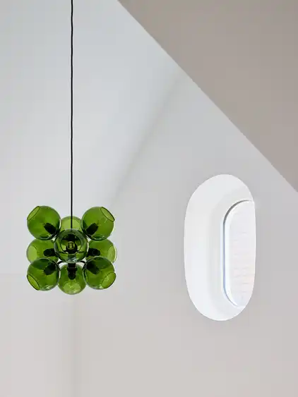 Grüne Designlampe vor einer weißen Wand mit Fenster