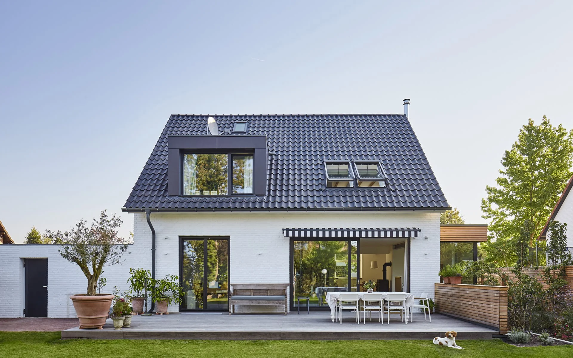 zweistöckiges weißes Haus mit dunkelblauem Spitzdach, Terrasse, Garten am Tag