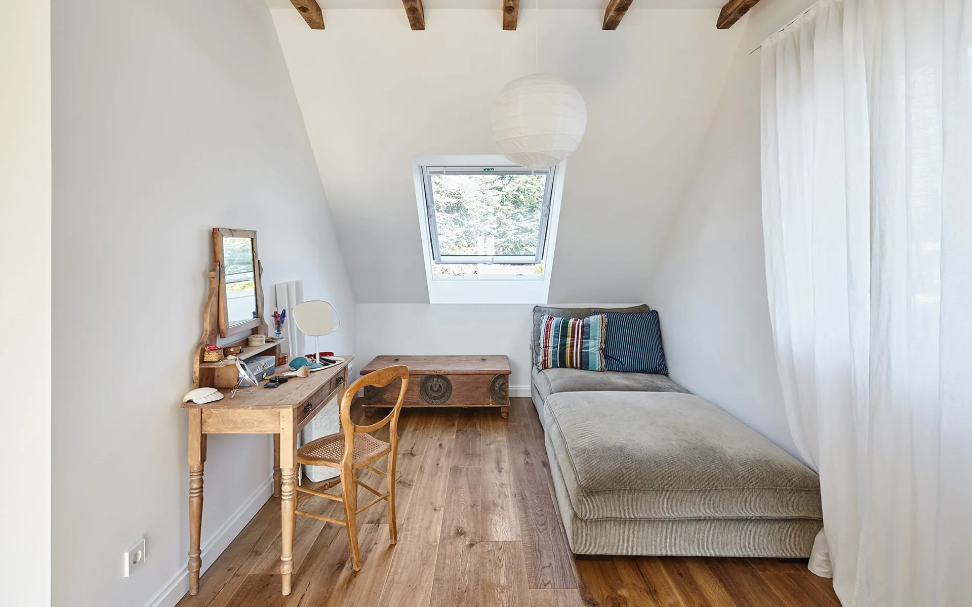 kleines Zimmer mit Schlafsofa rechts und Schreibtisch links, Blick auf ein Dachfenster
