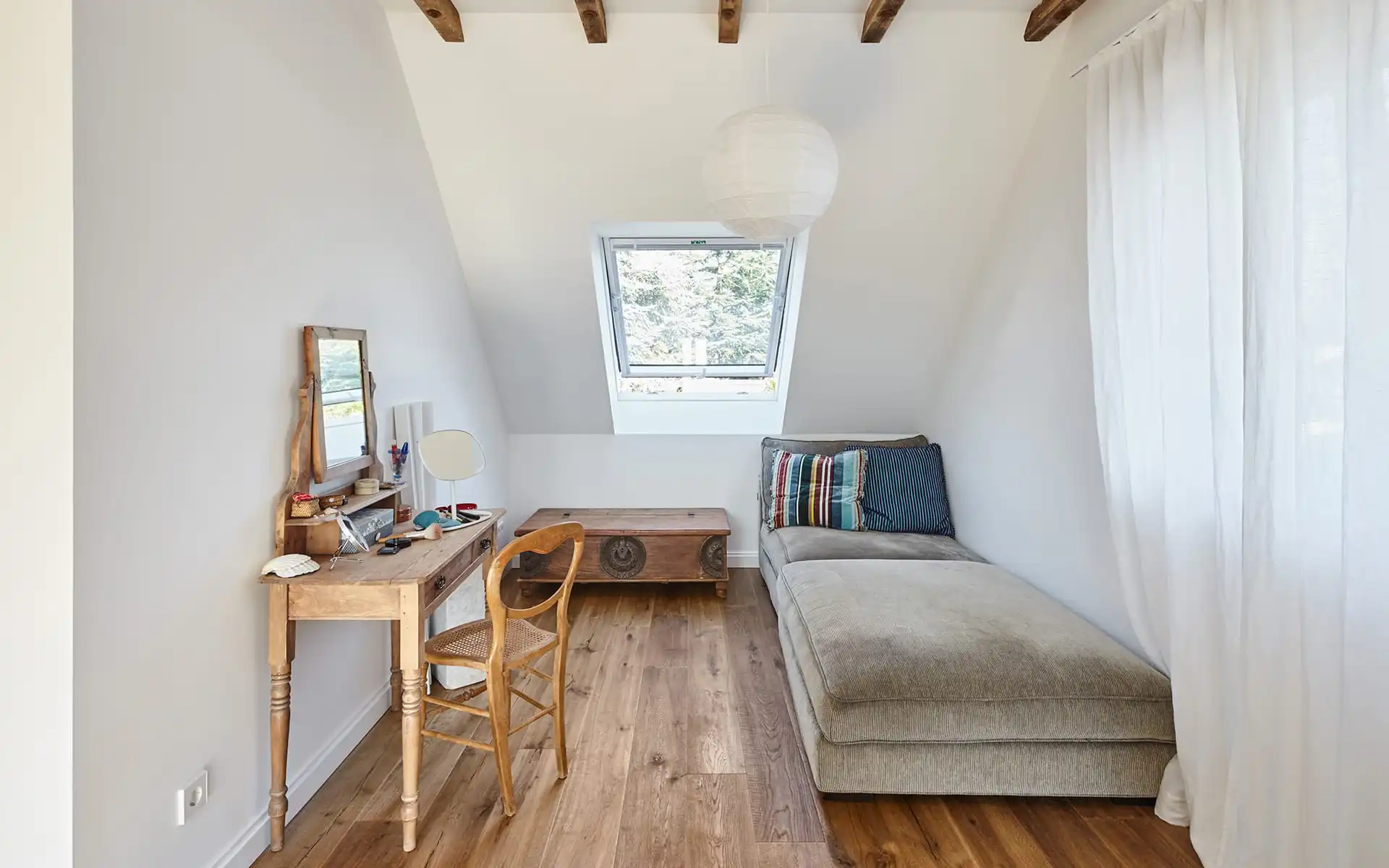 kleines Zimmer mit Schlafsofa rechts und Schreibtisch links, Blick auf ein Dachfenster