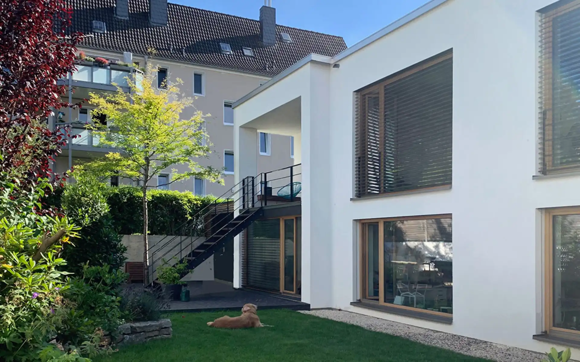 zweistöckiges weißes Haus mit großen Fenstern und Aussentreppe in den Garten