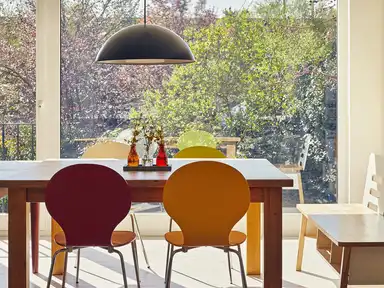 Tischgarnitur mit Holztisch und bunten Stühlen, Blick durch Fensterfront auf Garten