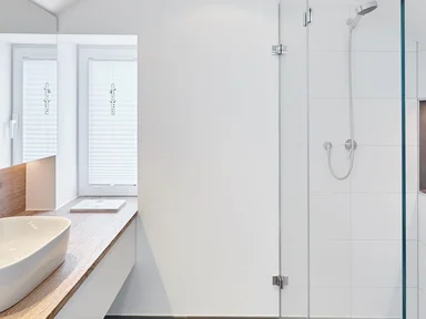 helles weißes Badezimmer mit Waschbecken links, Glasdusche rechts