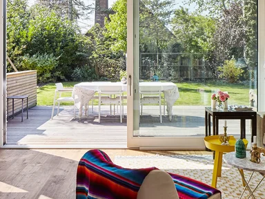 Wohnzimmer mit Sofa rechts und Blick auf Fensterfront zur Terrasse hinaus