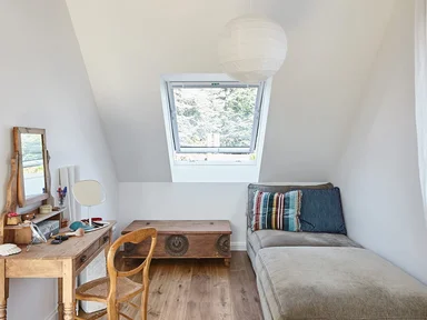 kleines Zimmer mit Schlafsofa rechts und Schreibtisch links, Blick auf ein Dachfenster