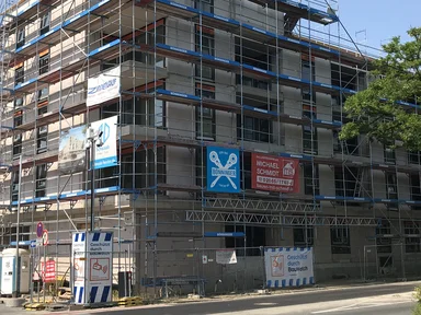 mehrstöckiges unfertiges Gebäude mit Bauzaun, Blick von der Straße aus