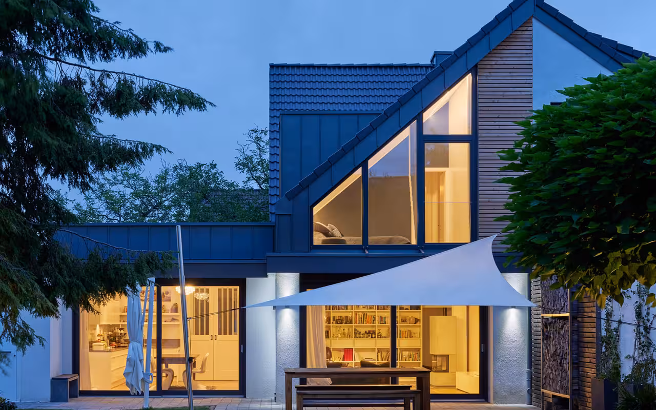 doppelstöckiges Gebäude mit Fensterfront: Sicht aus dem Garten am Abend