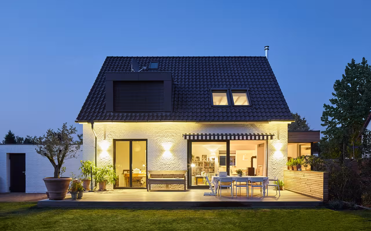 Zweistöckiges weißes Haus mit dunkelblauem Spitzdach und Garten