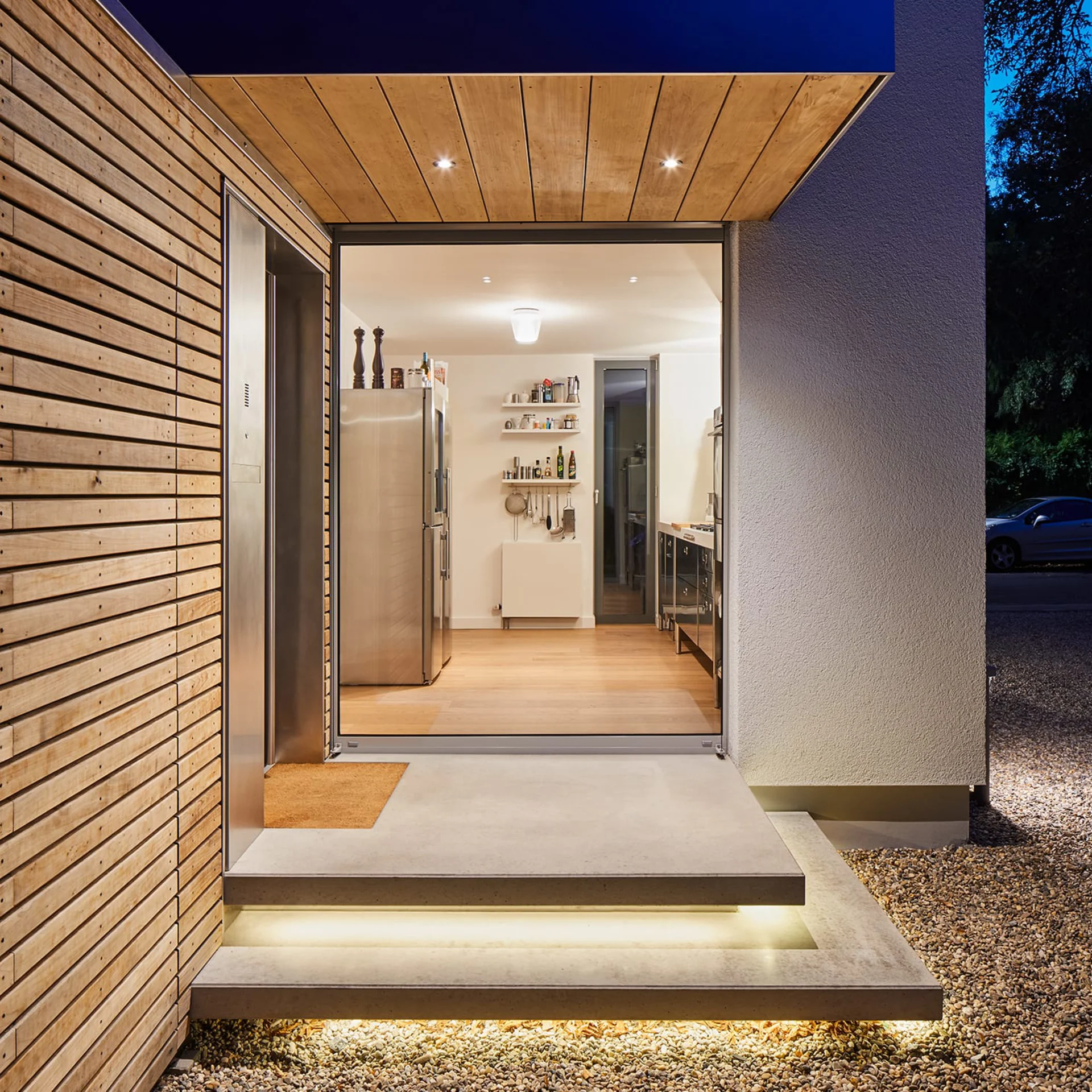 Eingang eines Hauses mit Holzfassade mit Blick in die Küche am Abend