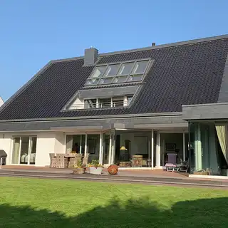 Dreistöckiges weißes Haus mit dunklem Spitzdach über zwei Etagen